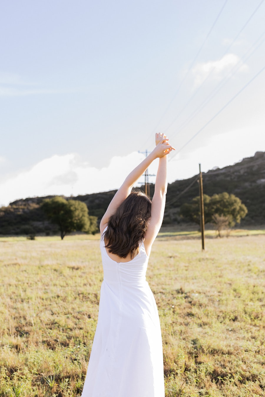 Woman in a white dress stretching her arms up to a bright sky